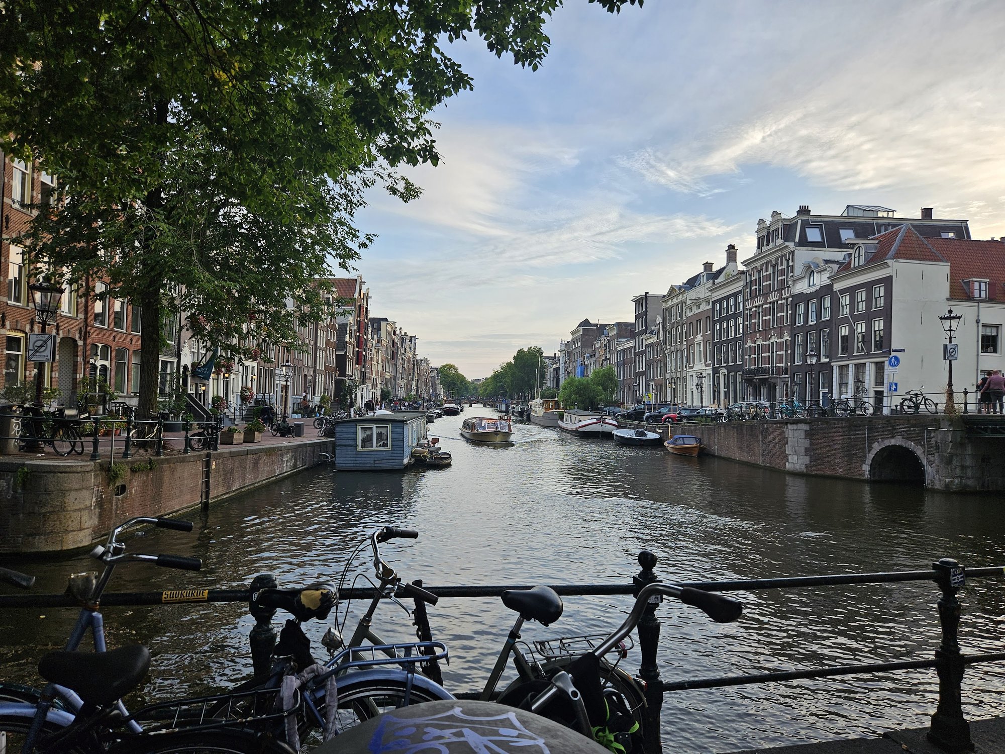 Amsterdam canal at dusk — bikes, houseboats, tour boat