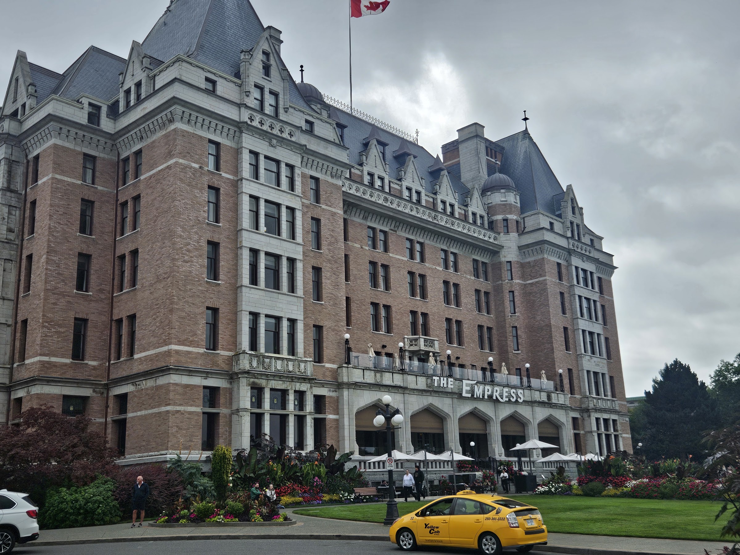 The ivy-free brick facade of the Fairmont Empress hotel with a yellow cab out front